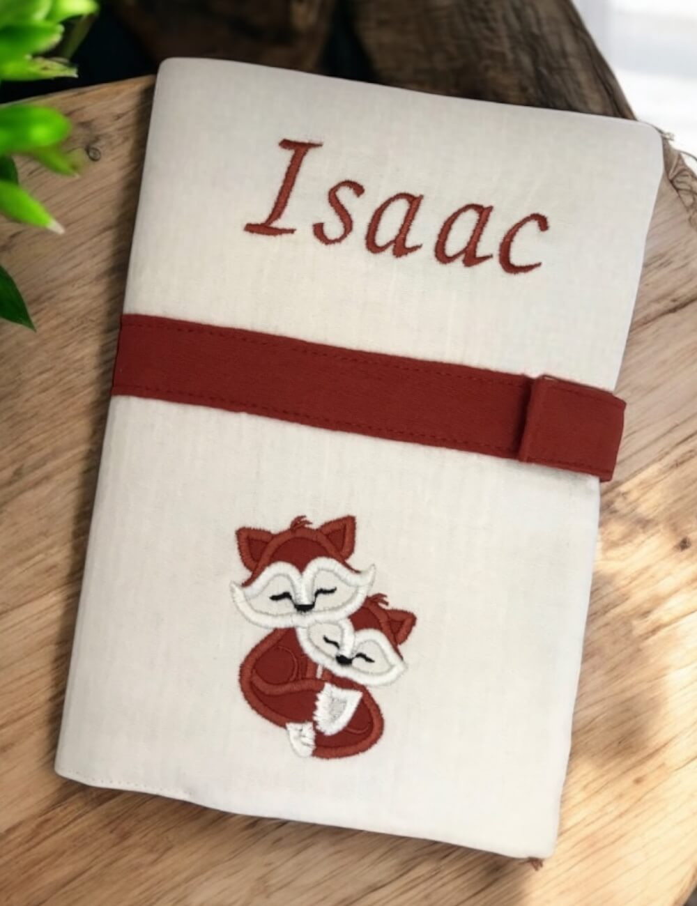 Protège carnet de santé bébé en double gaze de coton écrue brodé avec le prénom Isaac et un motif de renard.